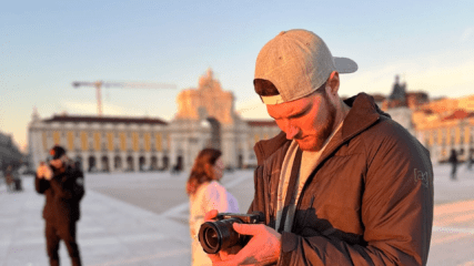 A man stands in a plaza and looks at a camera.